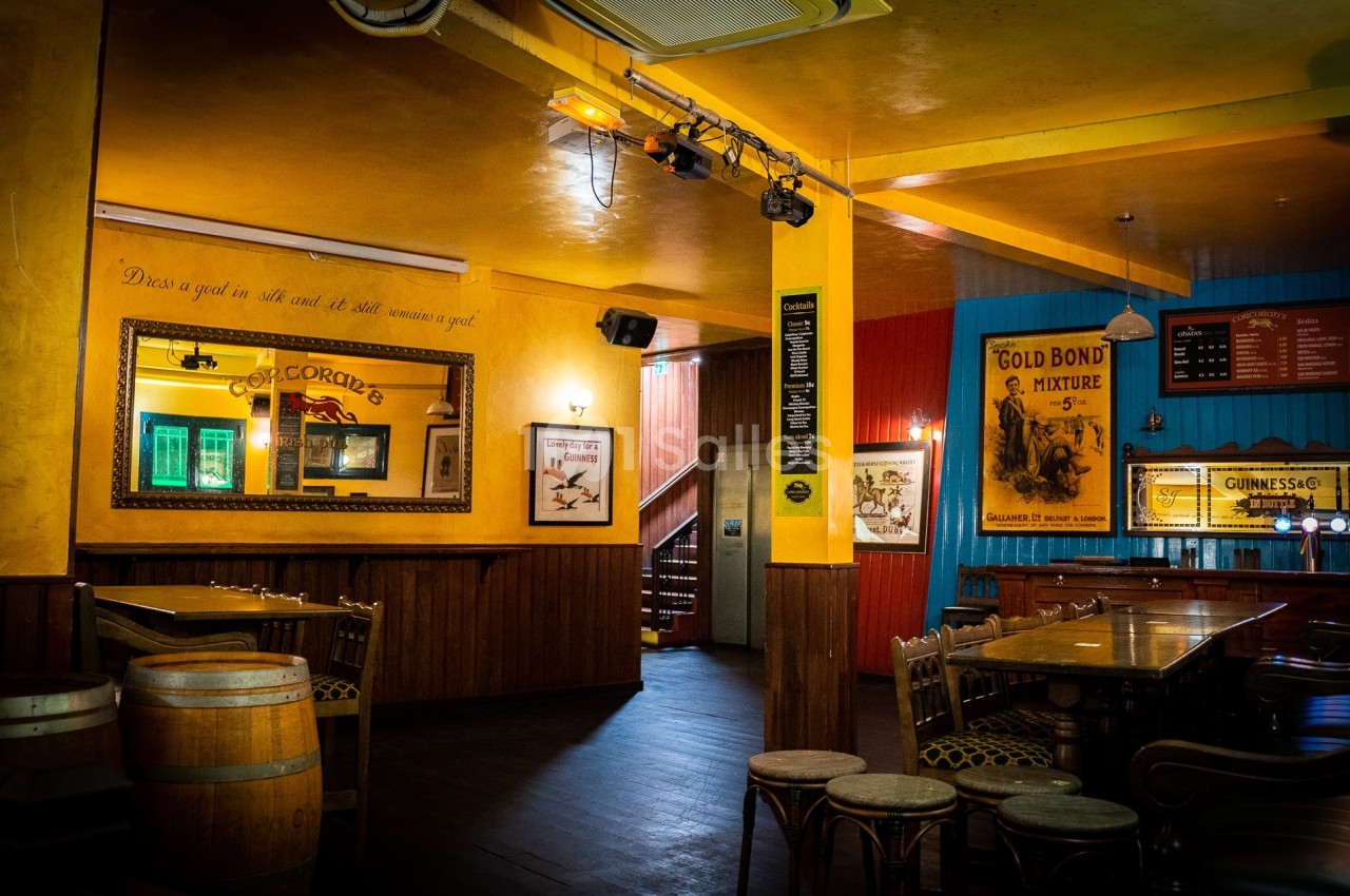 Intérieur d'un pub chaleureux avec des murs colorés, des tables en bois et des affiches décoratives vintage.