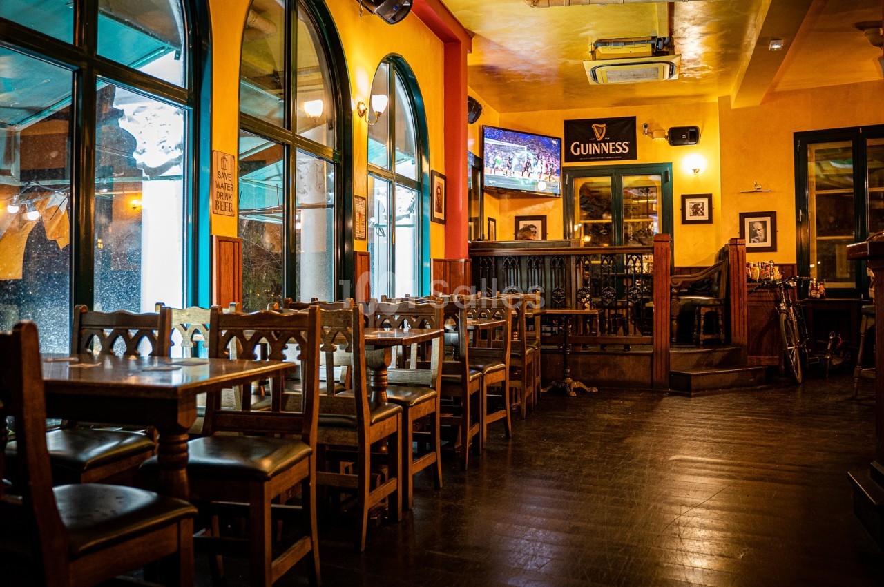 Intérieur d'un pub chaleureux avec des tables en bois, des chaises alignées et un bar en arrière-plan.