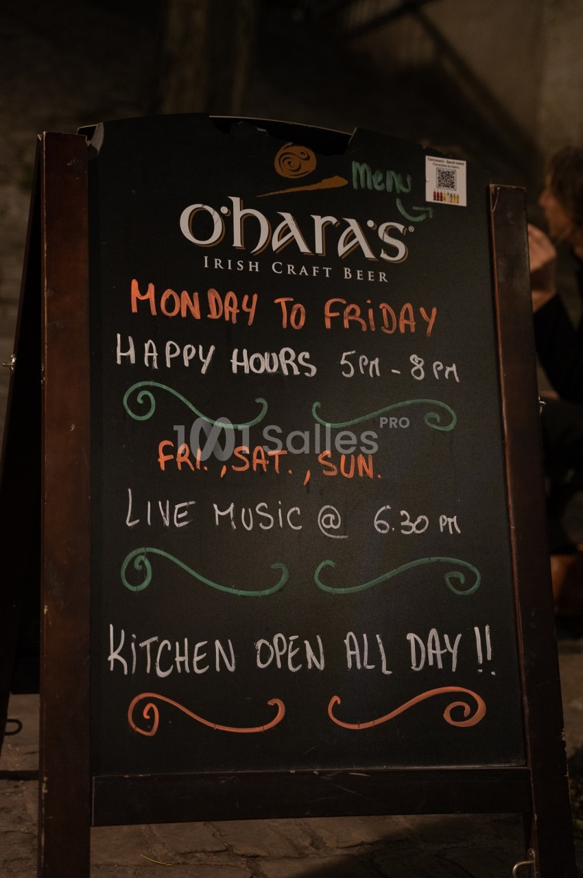 Tableau noir annonçant les horaires des happy hours, musique live et disponibilité de la cuisine dans un bar.
