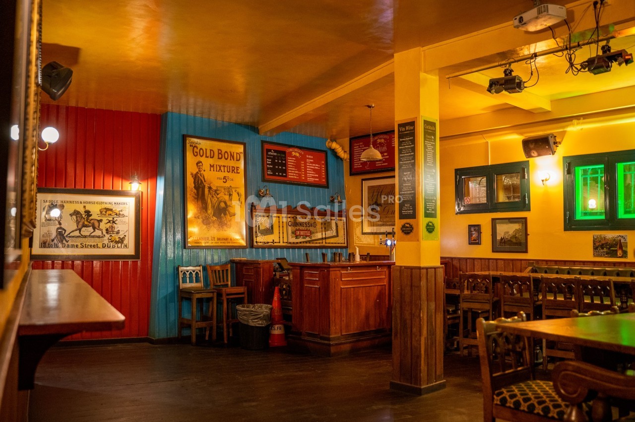 Intérieur d'un pub chaleureux avec des murs colorés, des affiches vintage, un bar en bois et des tables en bois.