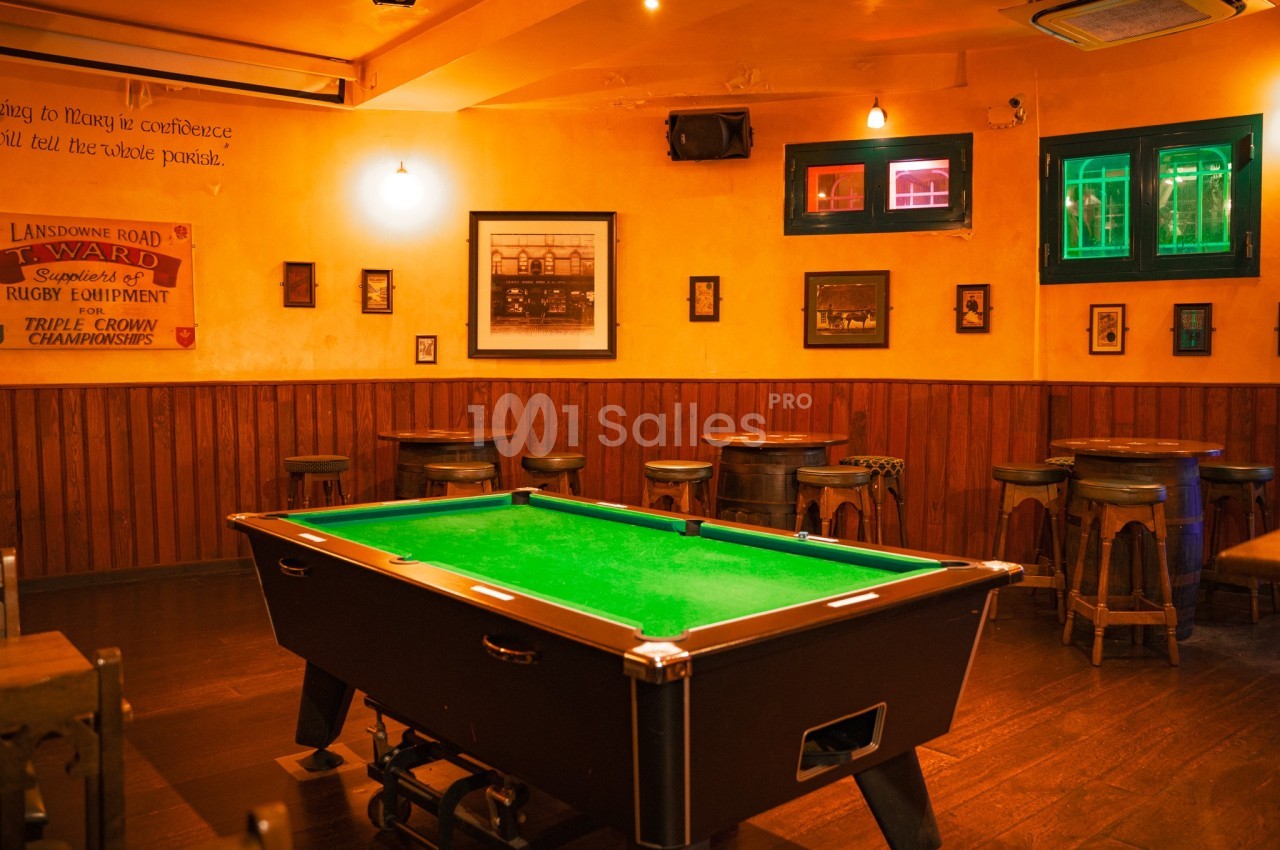 Table de billard noire avec tapis vert dans un bar à l'ambiance chaleureuse, éclairé par des lumières tamisées.