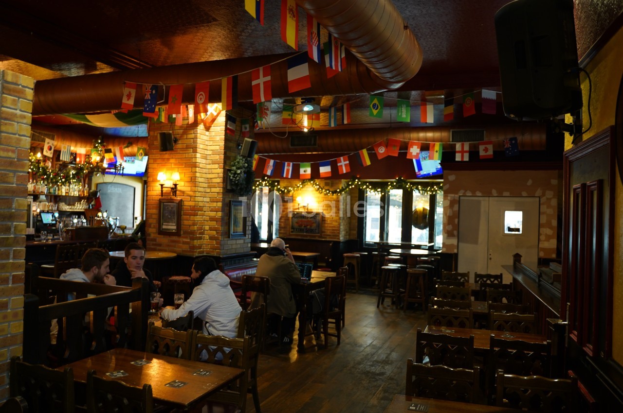 Intérieur d'un pub avec des drapeaux suspendus, des tables en bois et quelques clients assis.