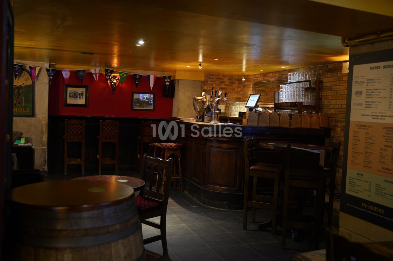 Intérieur d'un pub avec un comptoir en bois, des tabourets hauts, des décorations murales et un éclairage tamisé.