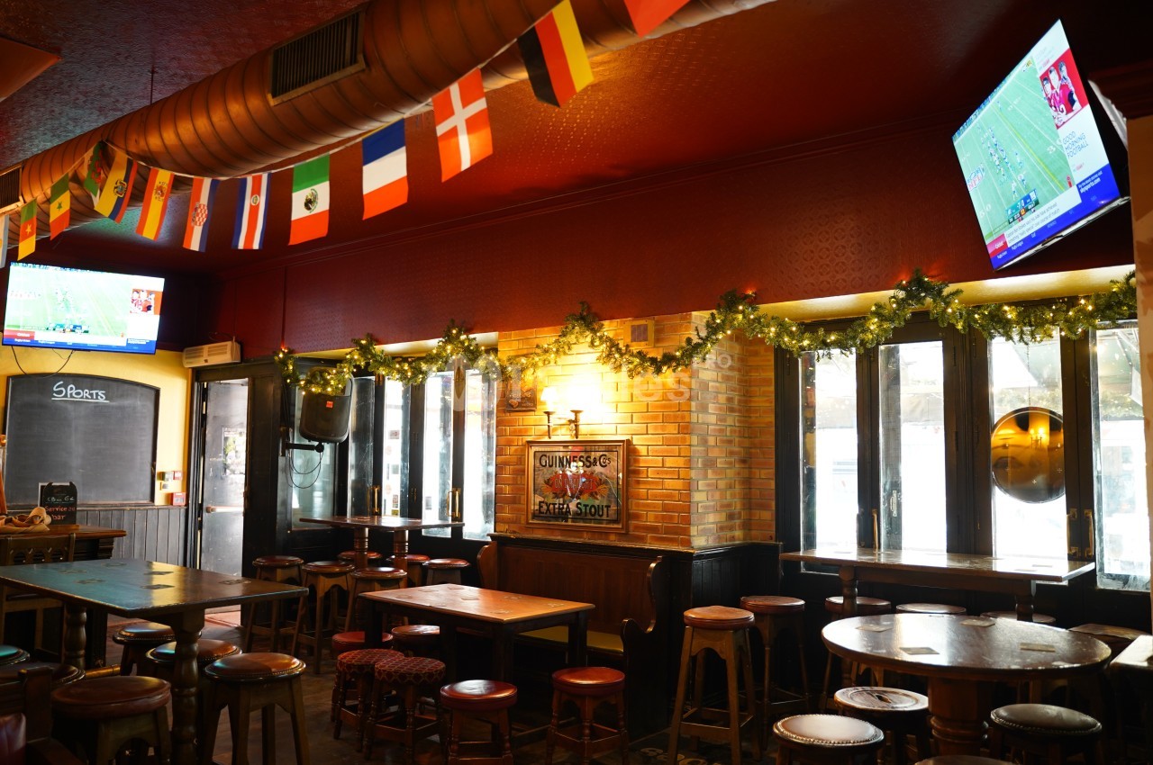 Intérieur d'un pub décoré de guirlandes lumineuses, avec des drapeaux suspendus et des écrans diffusant des matchs.