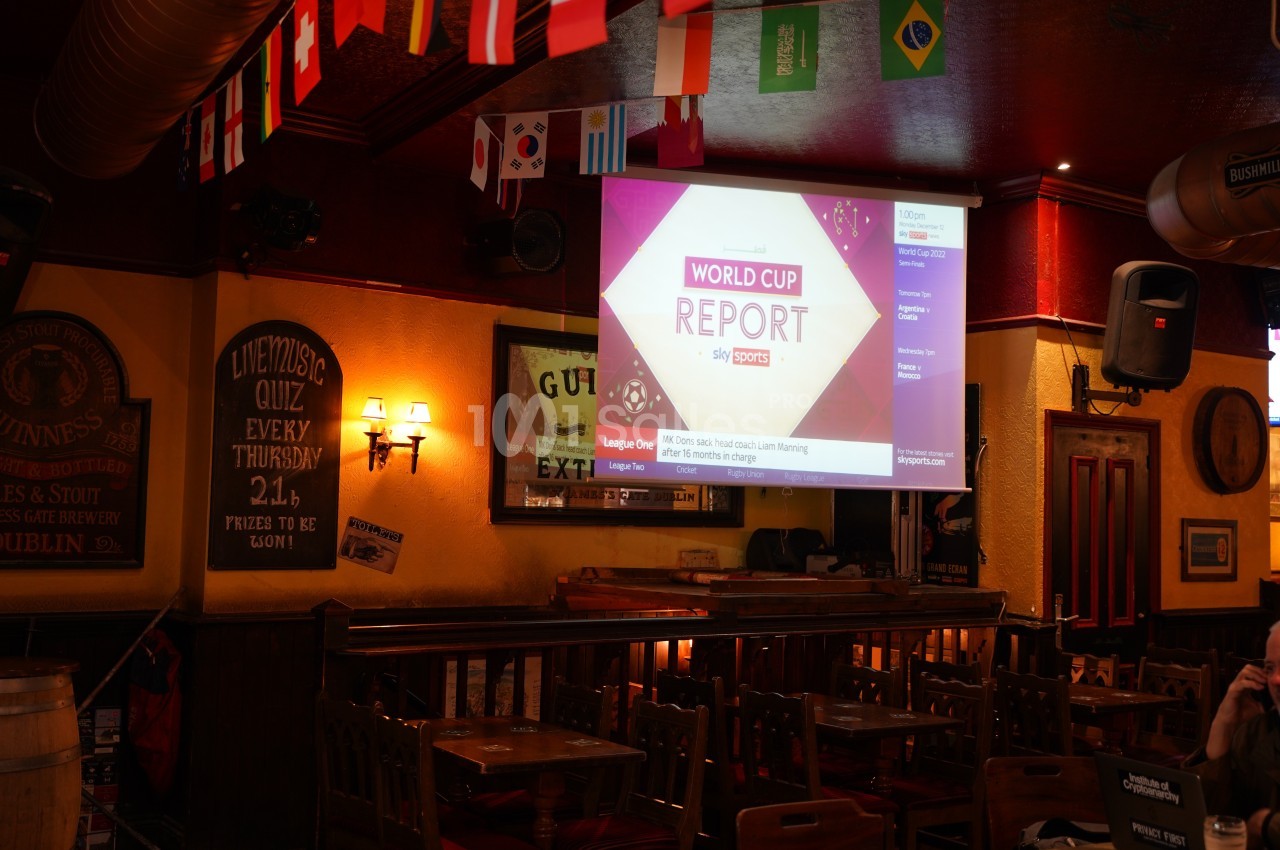 Intérieur d'un pub avec des drapeaux suspendus et un écran affichant un rapport sur la Coupe du Monde.