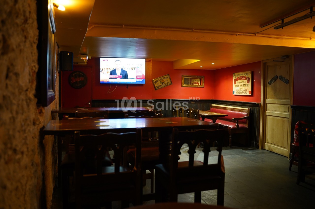 Salle de restaurant vide avec des tables en bois, murs rouges décorés et un écran diffusant une émission.