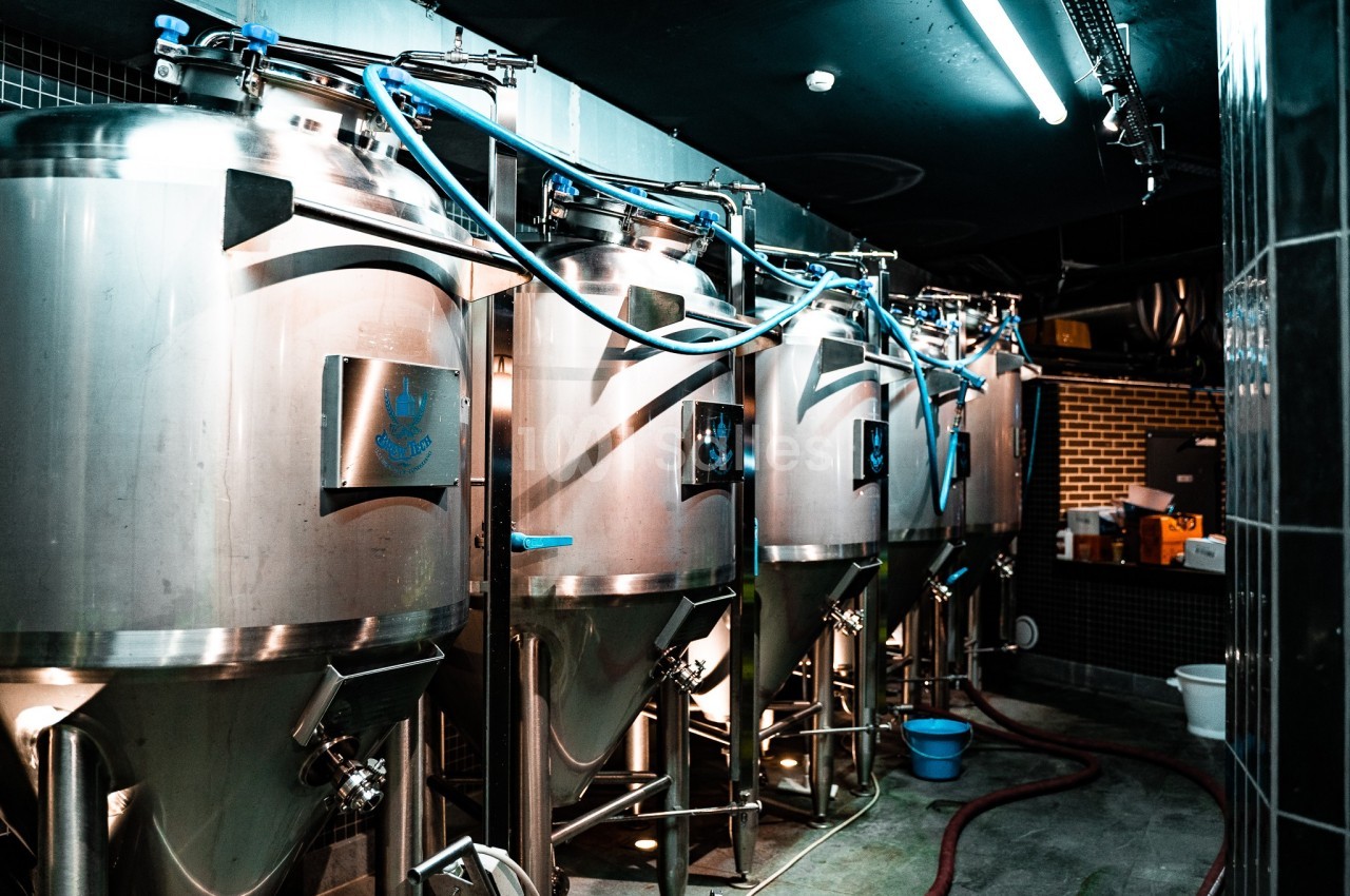 Cuves en acier inoxydable alignées dans une brasserie, reliées par des tuyaux pour le processus de fermentation.