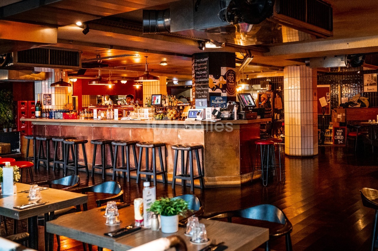 Intérieur d'un restaurant avec un bar central, des tabourets hauts, des tables dressées et une ambiance chaleureuse.