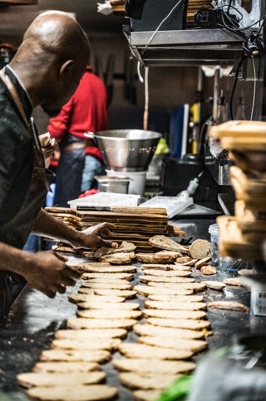 Un cuisinier dispose des tranches de pain sur un plan de travail dans une cuisine professionnelle.