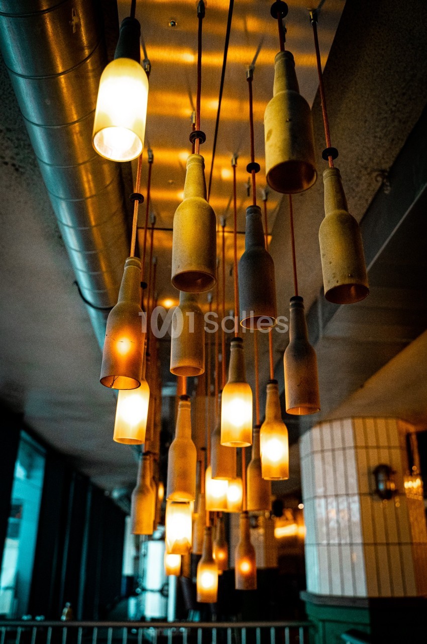 Suspension lumineuse composée de bouteilles recyclées éclairées, accrochées au plafond dans un intérieur moderne.