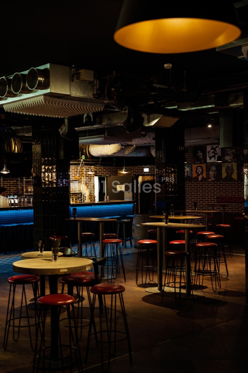 Salle de bar avec tables hautes, tabourets rouges et éclairage tamisé, décor industriel en arrière-plan.