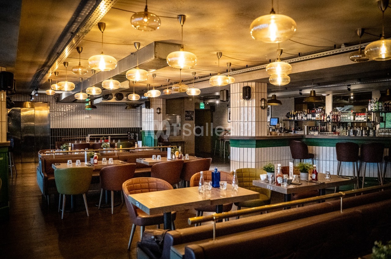 Salle de restaurant moderne avec tables en bois, chaises colorées et éclairage suspendu chaleureux.