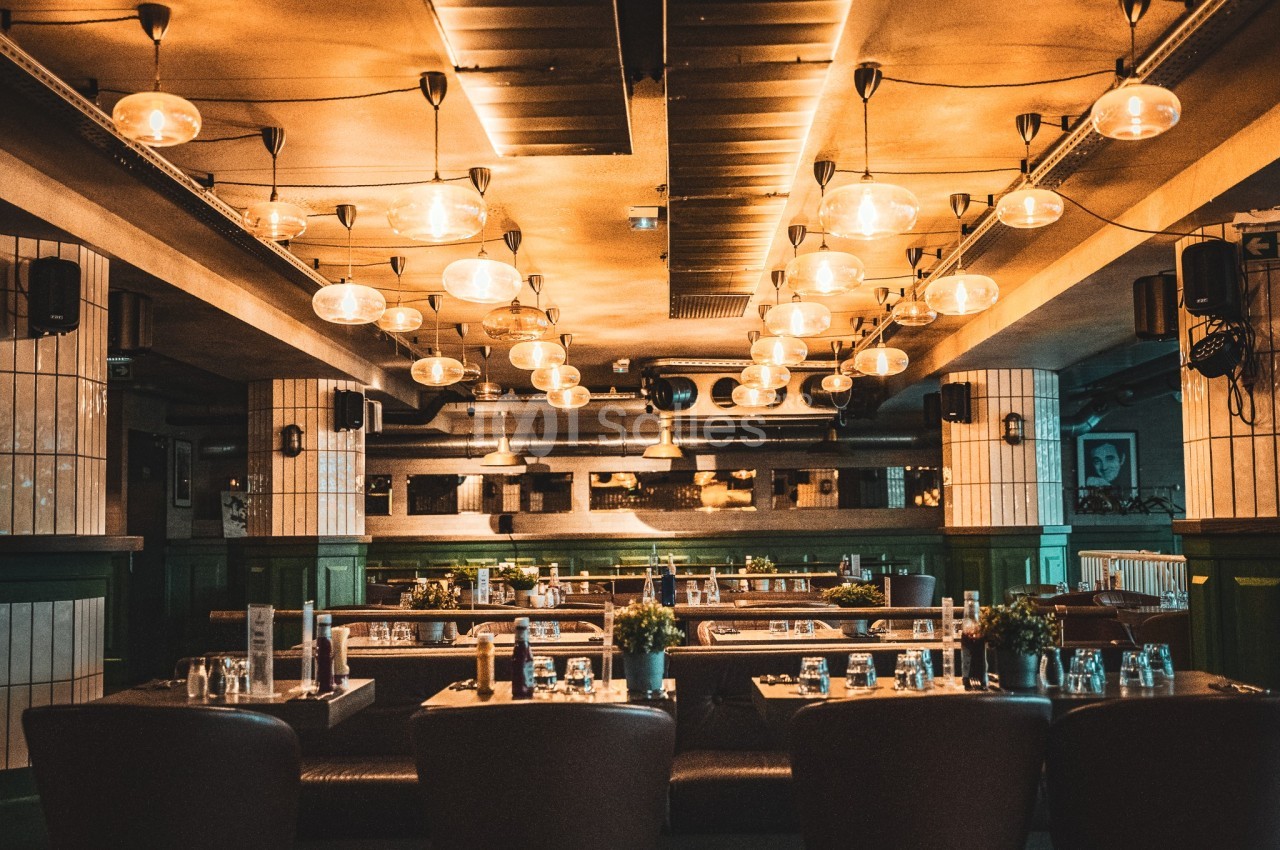 Salle de restaurant chaleureuse avec éclairage suspendu, tables dressées et décor industriel.