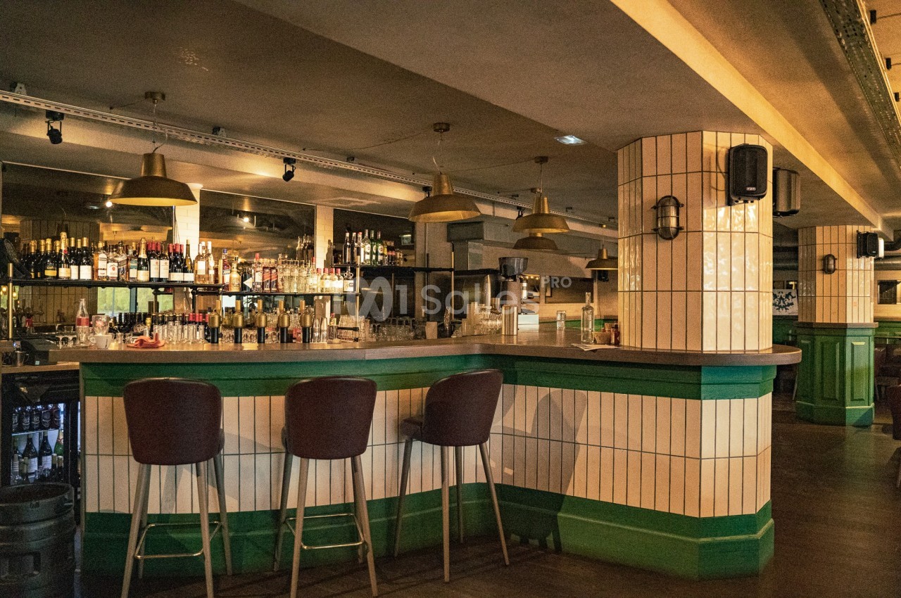 Bar avec comptoir en bois, tabourets hauts, étagères remplies de bouteilles et éclairage suspendu dans une ambiance…