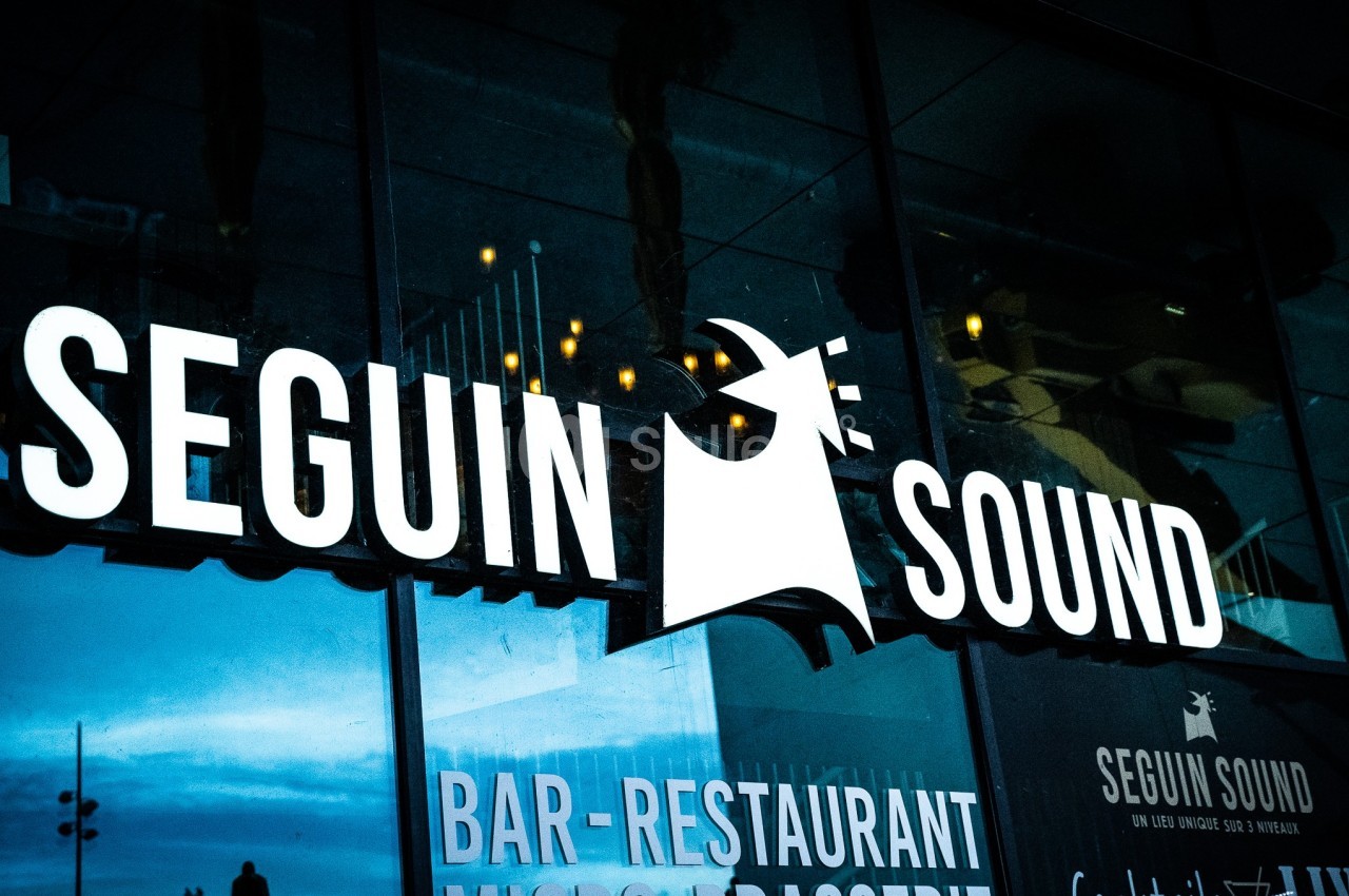 Façade vitrée avec le logo lumineux ’Seguin Sound’ et des inscriptions pour un bar-restaurant.