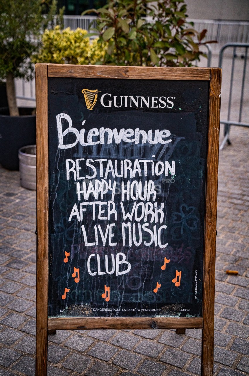 Tableau noir devant un établissement annonçant restauration, happy hour, musique live et club.