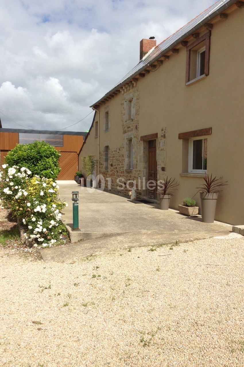 Façade d'une maison en pierre rénovée avec des jardinières, une allée en gravier et un portail en bois au fond.