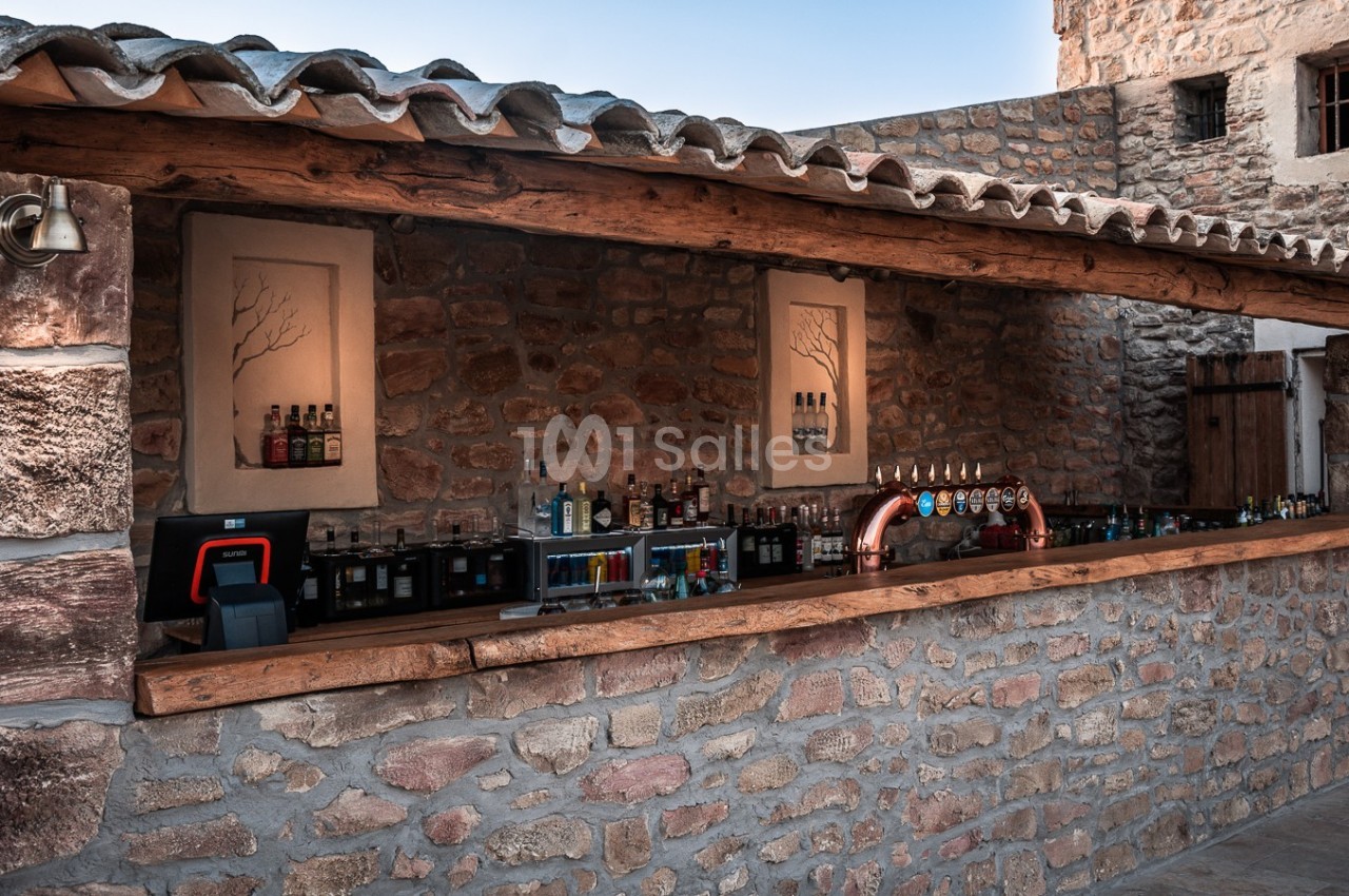 Bar extérieur en pierre avec comptoir en bois, équipé de tireuses à bière et de bouteilles alignées sur des étagères.
