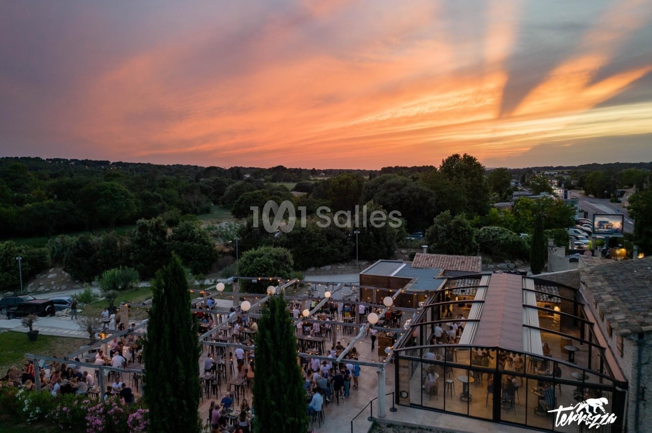 Vue aérienne d'une terrasse animée au coucher du soleil, entourée de verdure et de bâtiments modernes.