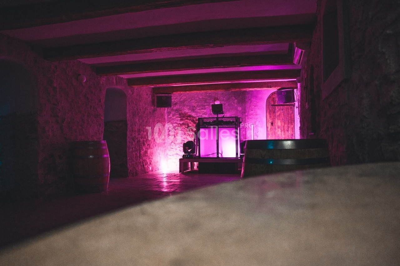 Salle en pierre avec éclairage rose, tonneaux en bois et équipement lumineux au fond.
