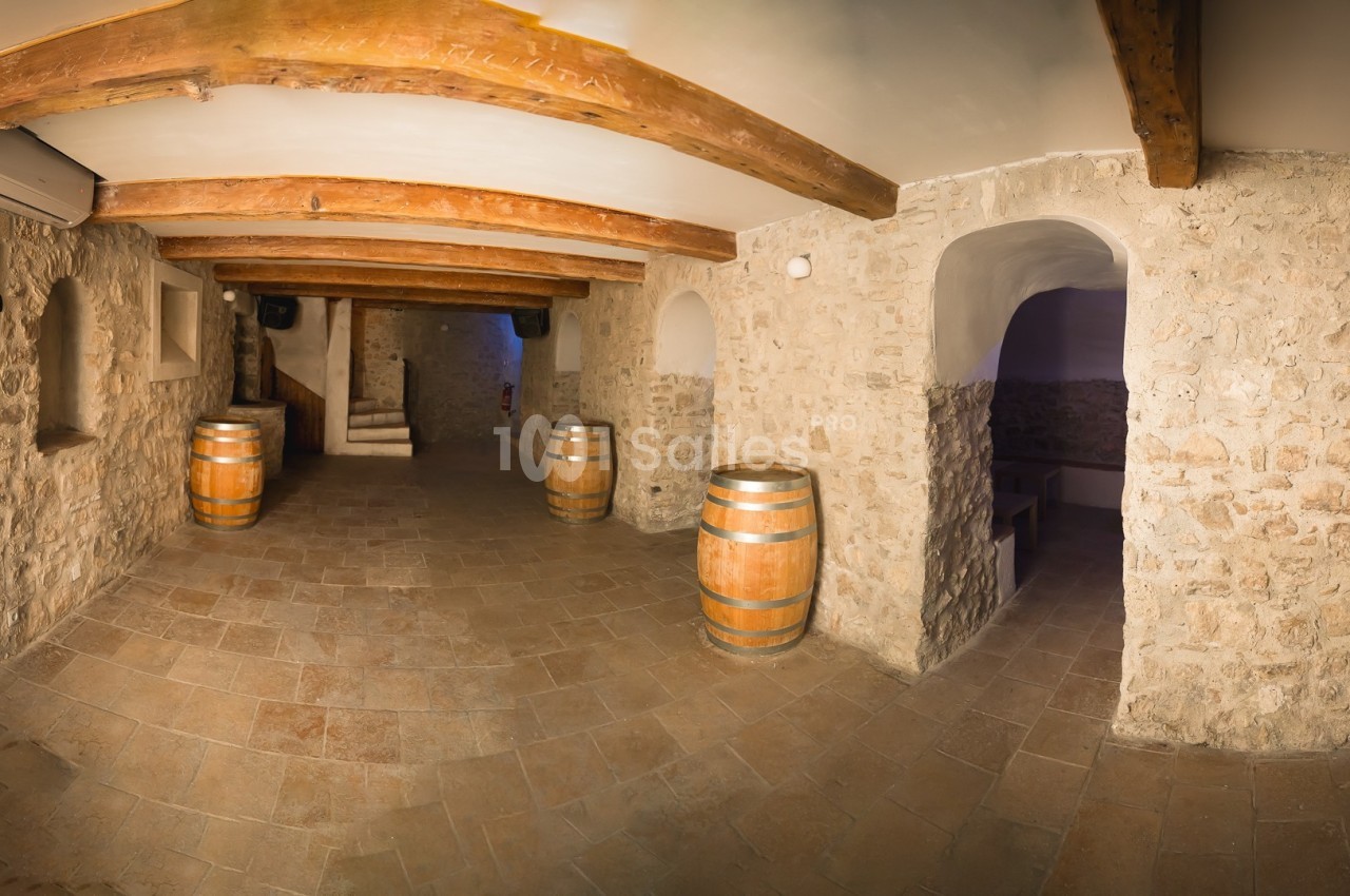 Salle voûtée en pierre avec des tonneaux en bois, un sol carrelé et des poutres apparentes au plafond.