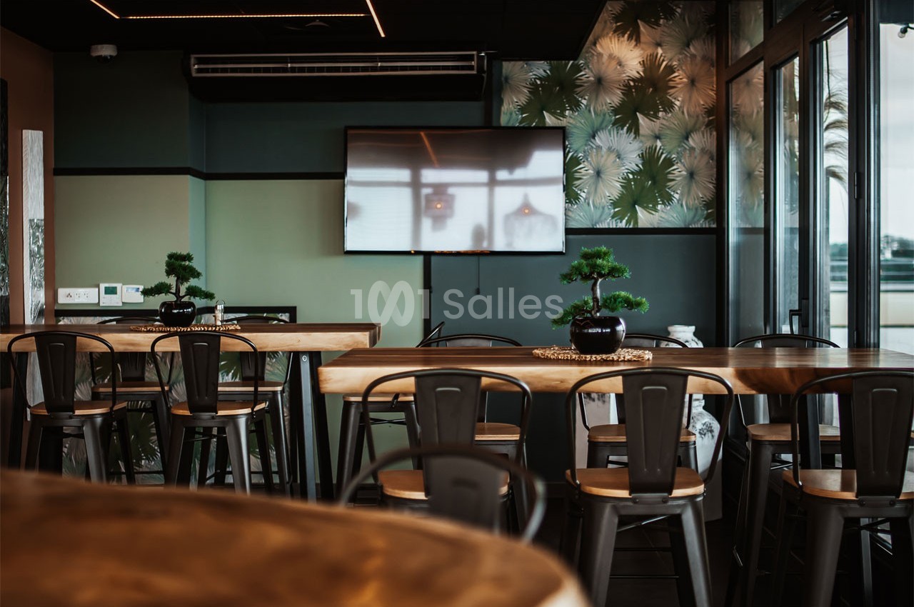 Salle de restaurant moderne avec tables en bois, chaises métalliques et plantes décoratives, éclairée par une grande baie…