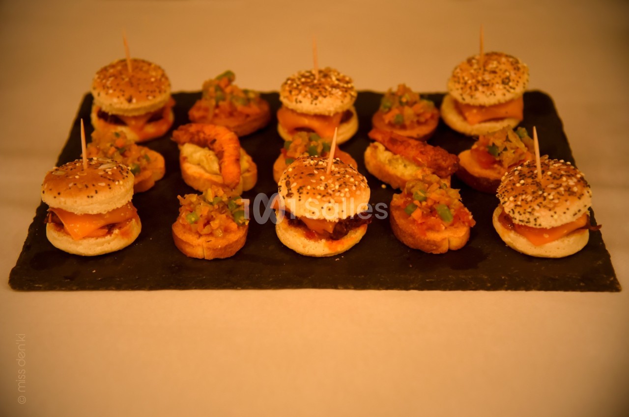 Plateau de mini-burgers et bouchées garnies de légumes et crevettes, disposés sur une ardoise noire.
