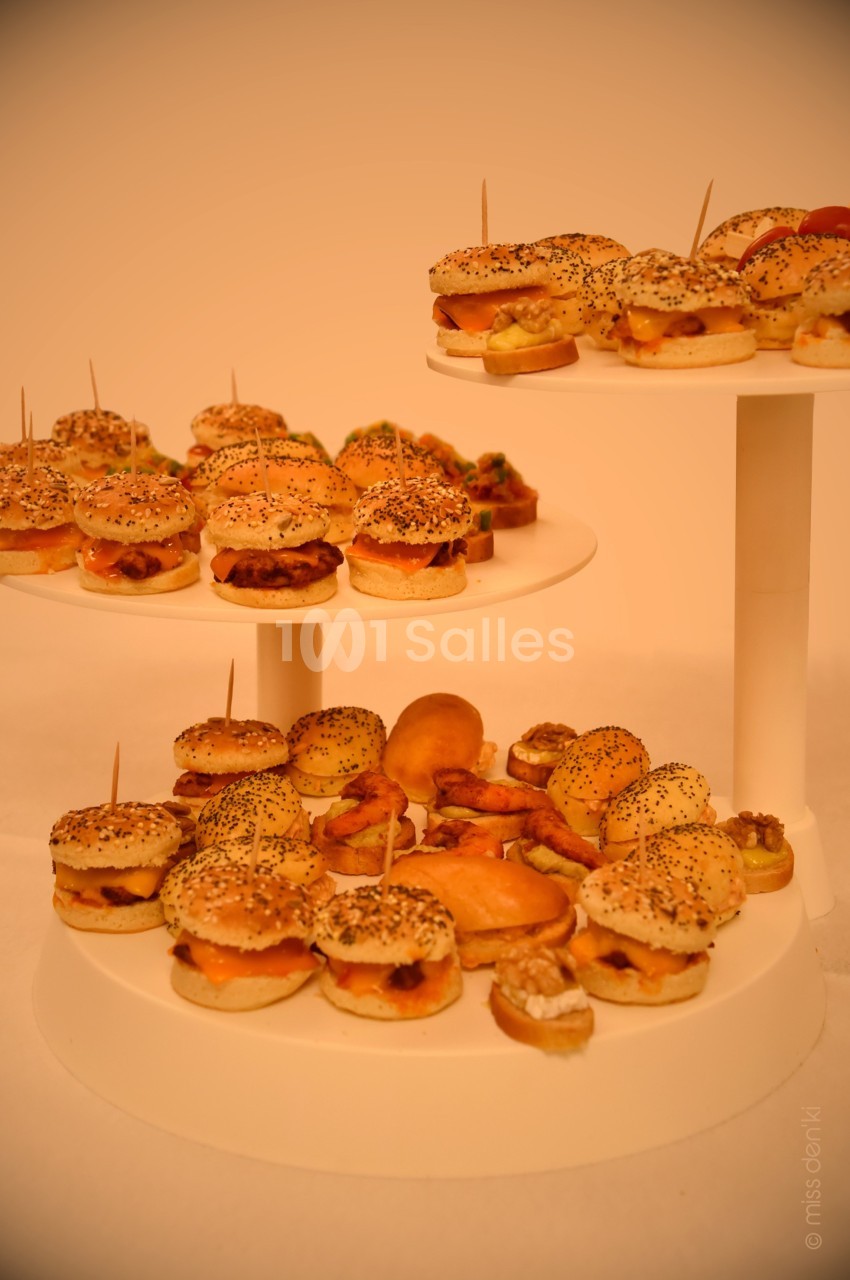 Plateaux de mini-burgers et amuse-bouches variés disposés sur des présentoirs blancs.