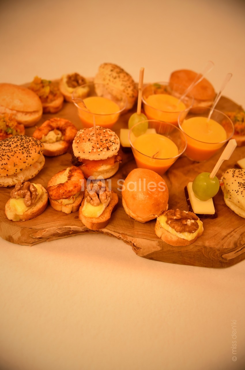 Plateau en bois garni de mini-burgers, verrines de soupe orange et amuse-bouches variés, dont des noix et raisins.