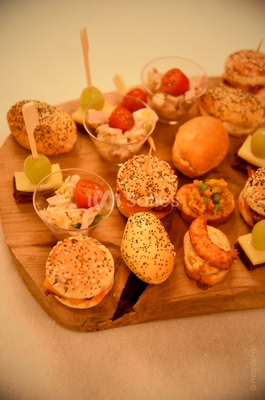 Plateau en bois garni de mini-sandwichs, verrines, bouchées salées et brochettes apéritives avec raisin et fromage.