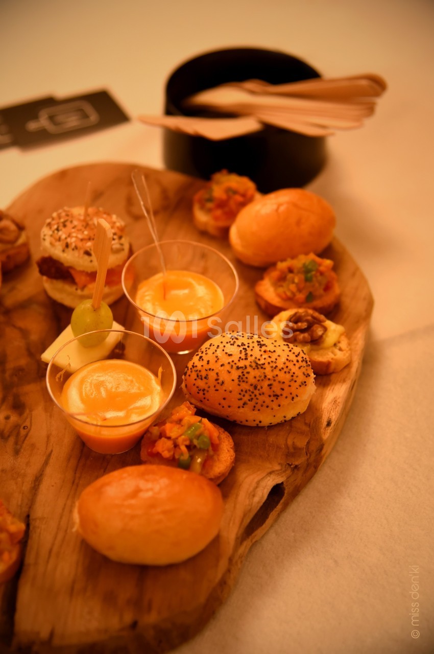 Plateau en bois avec des amuse-bouches variés, incluant verrines, pains garnis et bouchées salées, sur une table éclairée.