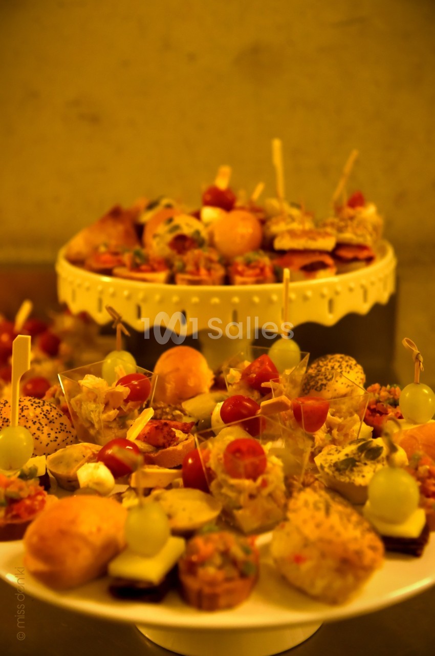Plateaux de bouchées apéritives variées avec légumes, fromages, pains et brochettes, disposés sur des présentoirs.