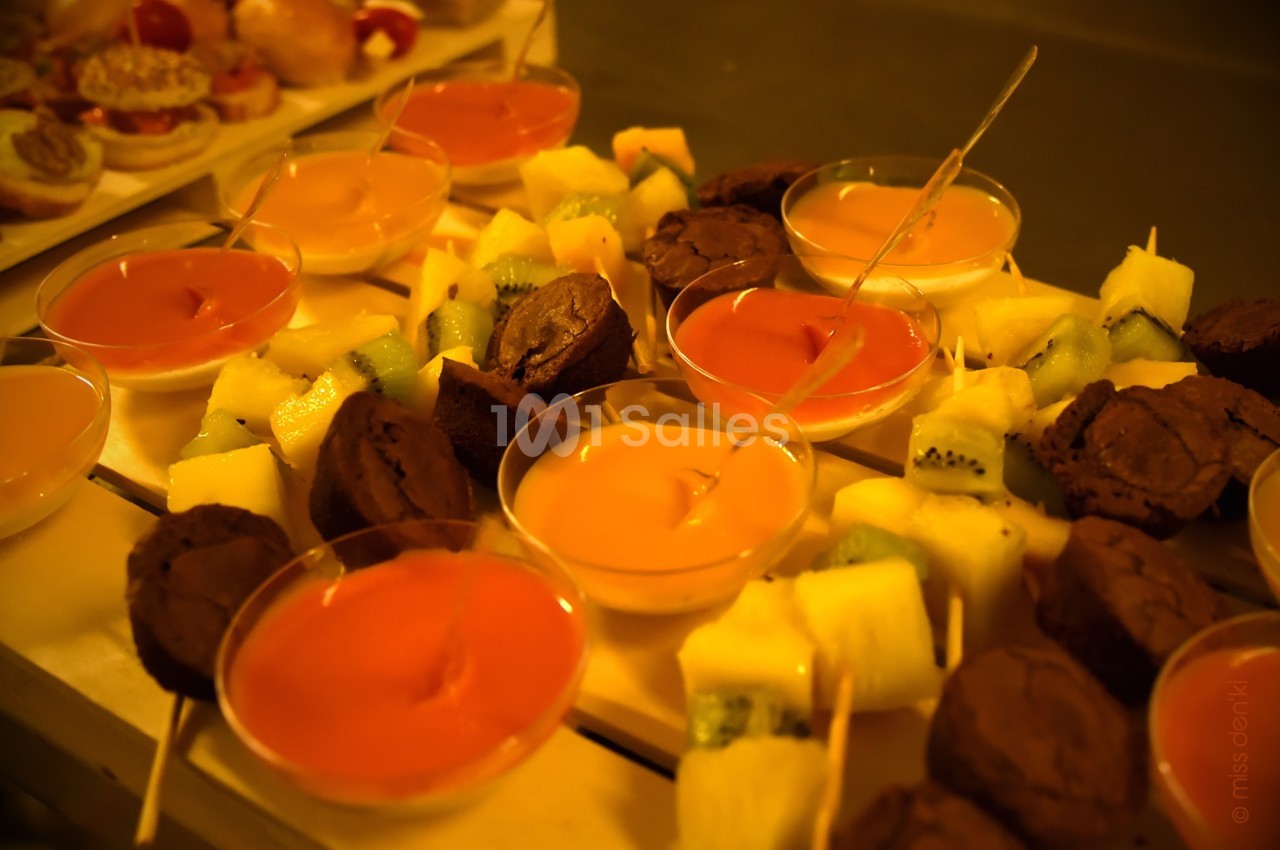 Assortiment de desserts comprenant brochettes de fruits, brownies et verrines colorées disposés sur une table.