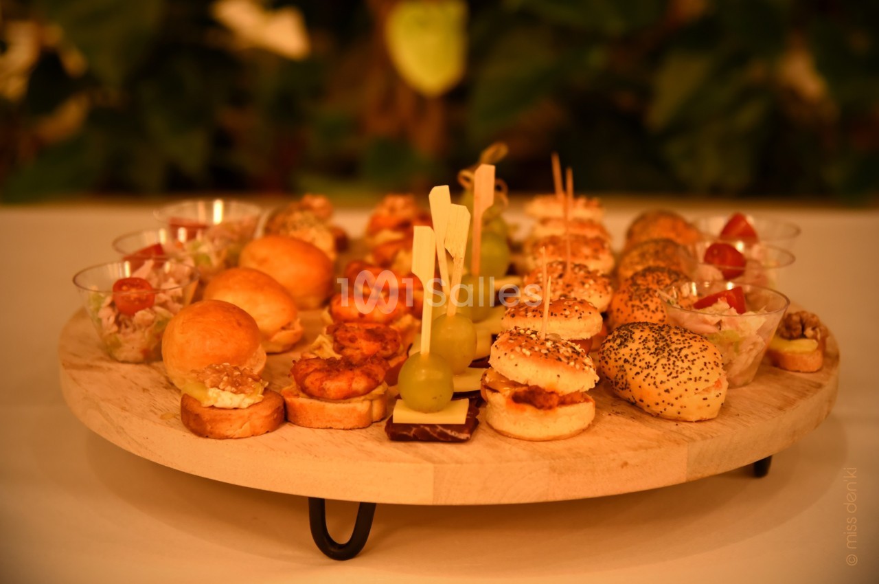 Plateau en bois garni de divers amuse-bouches, incluant mini-burgers, brochettes et verrines, présenté sur une table.