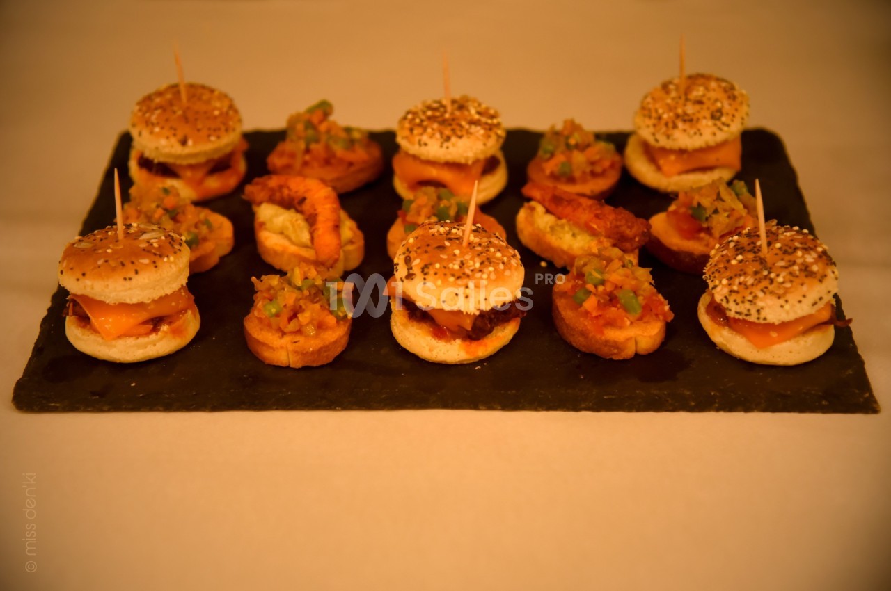 Plateau de mini-burgers et bouchées garnies de légumes et crevettes, disposés sur une ardoise noire.