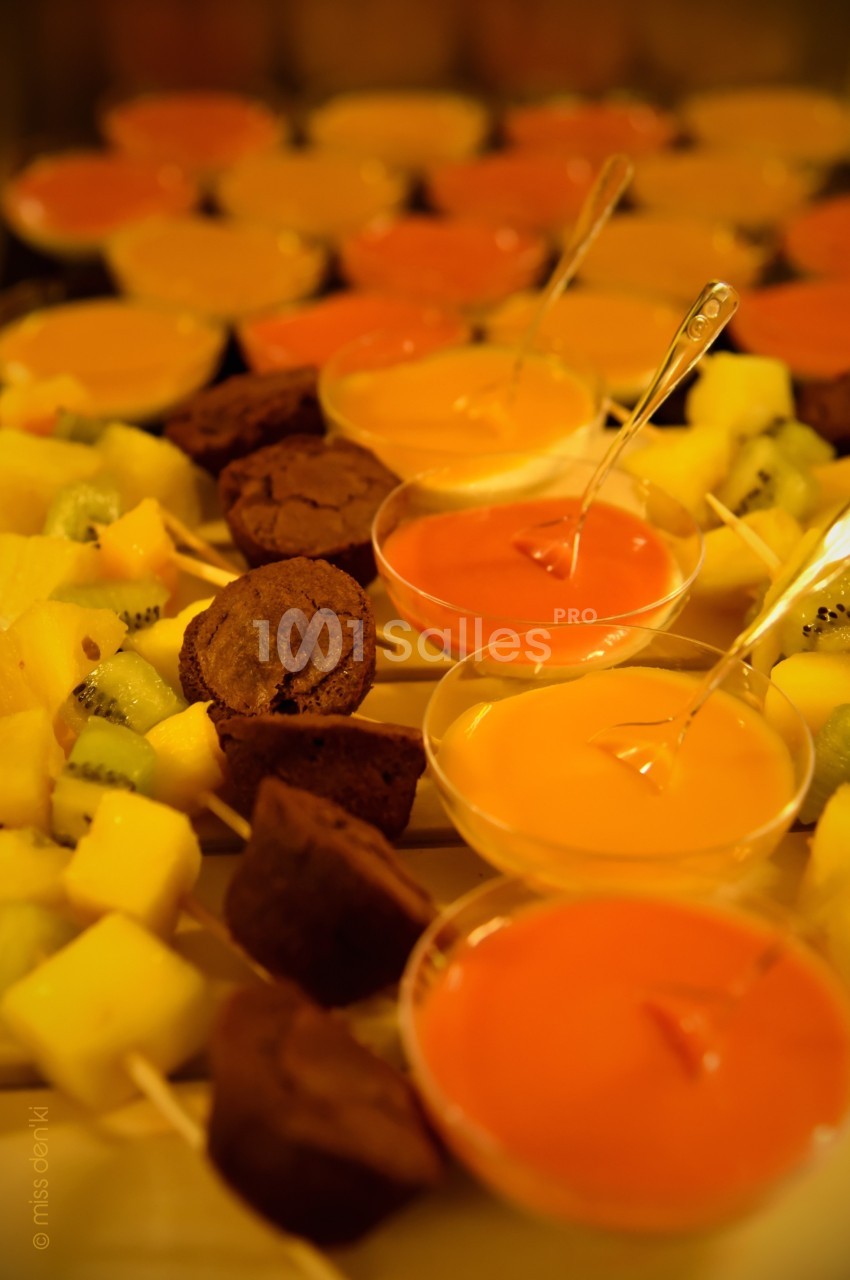 Brochettes de fruits et morceaux de gâteau accompagnés de verrines de sauces colorées sur une table.