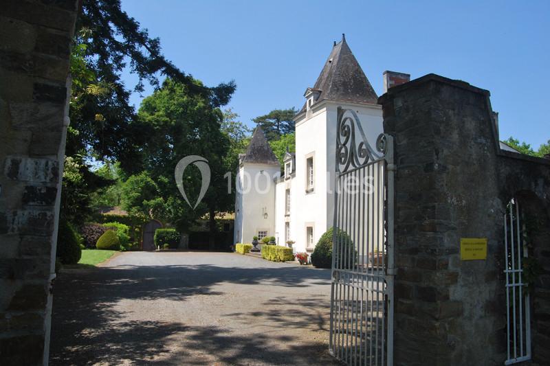 Entrée d'un domaine avec portail en fer forgé ouvert, menant à une bâtisse blanche entourée de végétation.