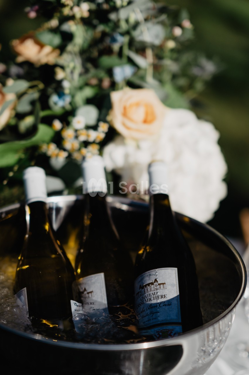 Bouteilles de vin blanc refroidissant dans un seau rempli de glace, avec des fleurs en arrière-plan.