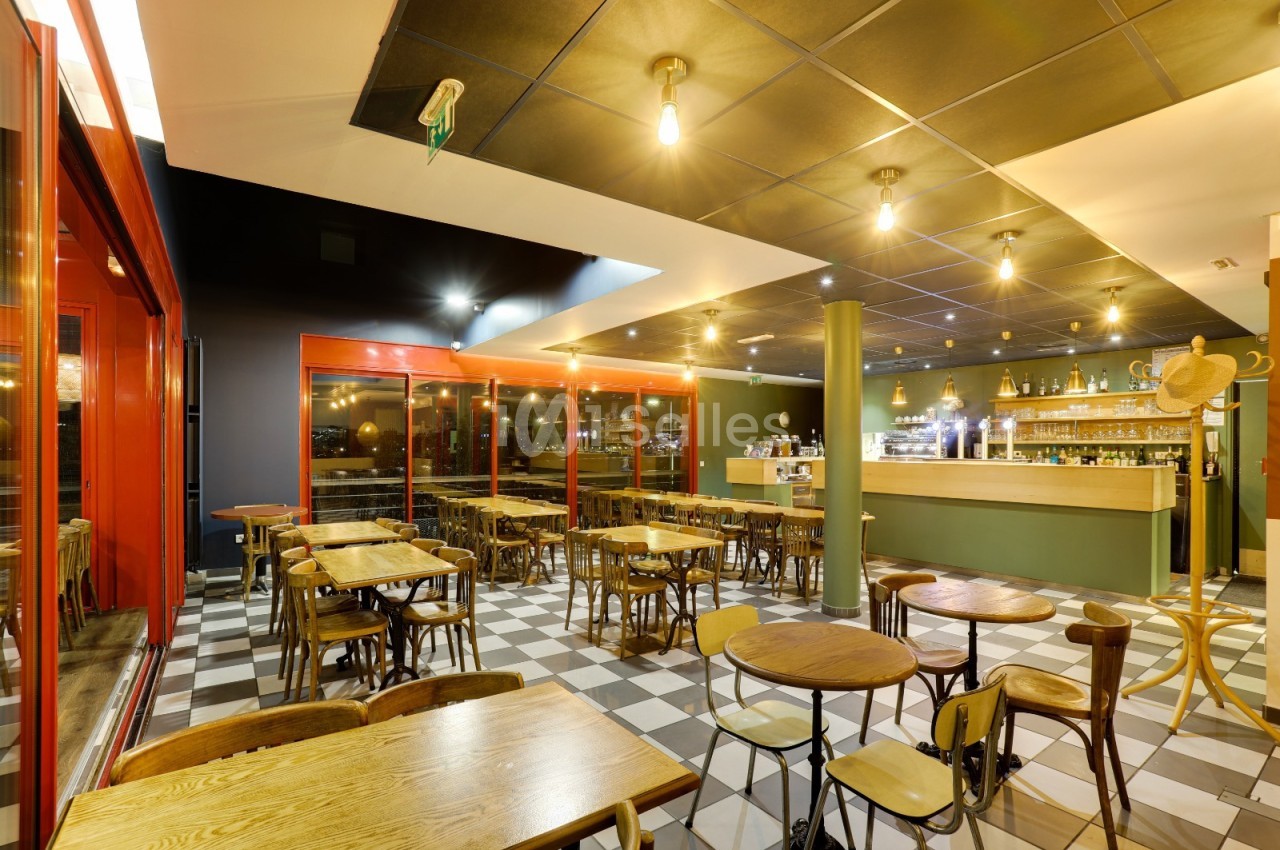 Salle de restaurant avec tables en bois, chaises assorties, éclairage suspendu et comptoir de bar en arrière-plan.
