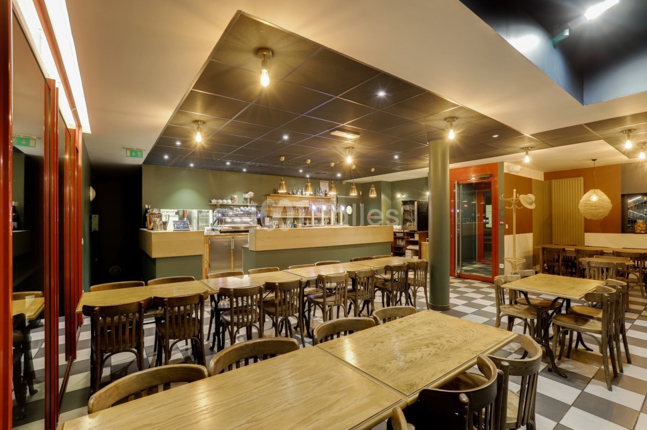 Salle de restaurant lumineuse avec tables en bois, chaises assorties et comptoir en arrière-plan.