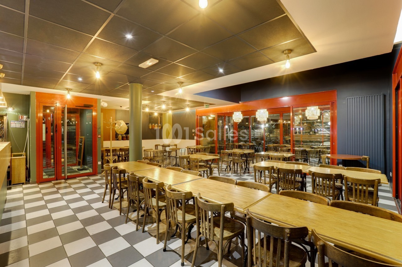 Salle de restaurant avec tables en bois, chaises assorties et éclairage chaleureux, sol en damier noir et blanc.