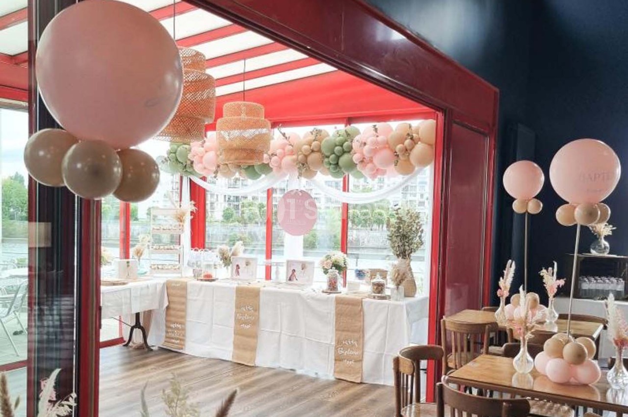 Décoration de salle avec ballons pastel et table dressée pour une réception, près de grandes baies vitrées.