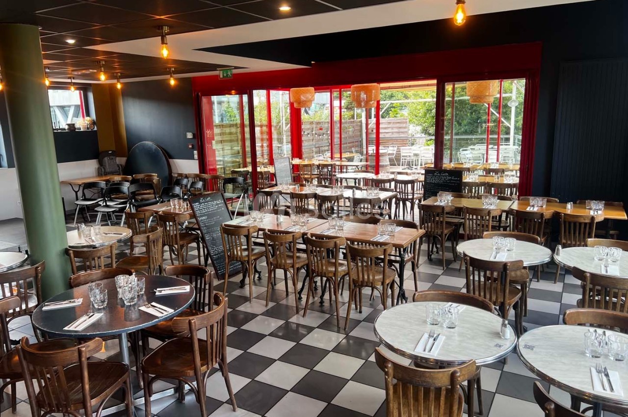 Salle de restaurant lumineuse avec des tables en marbre, des chaises en bois et une vue sur une terrasse extérieure.