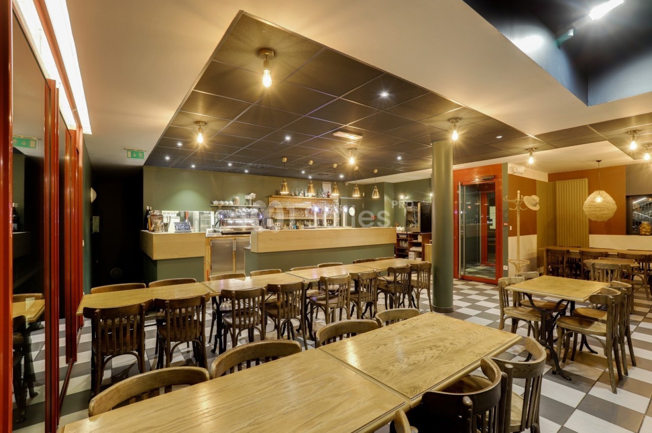 Salle de restaurant lumineuse avec tables en bois, chaises assorties et comptoir en arrière-plan.