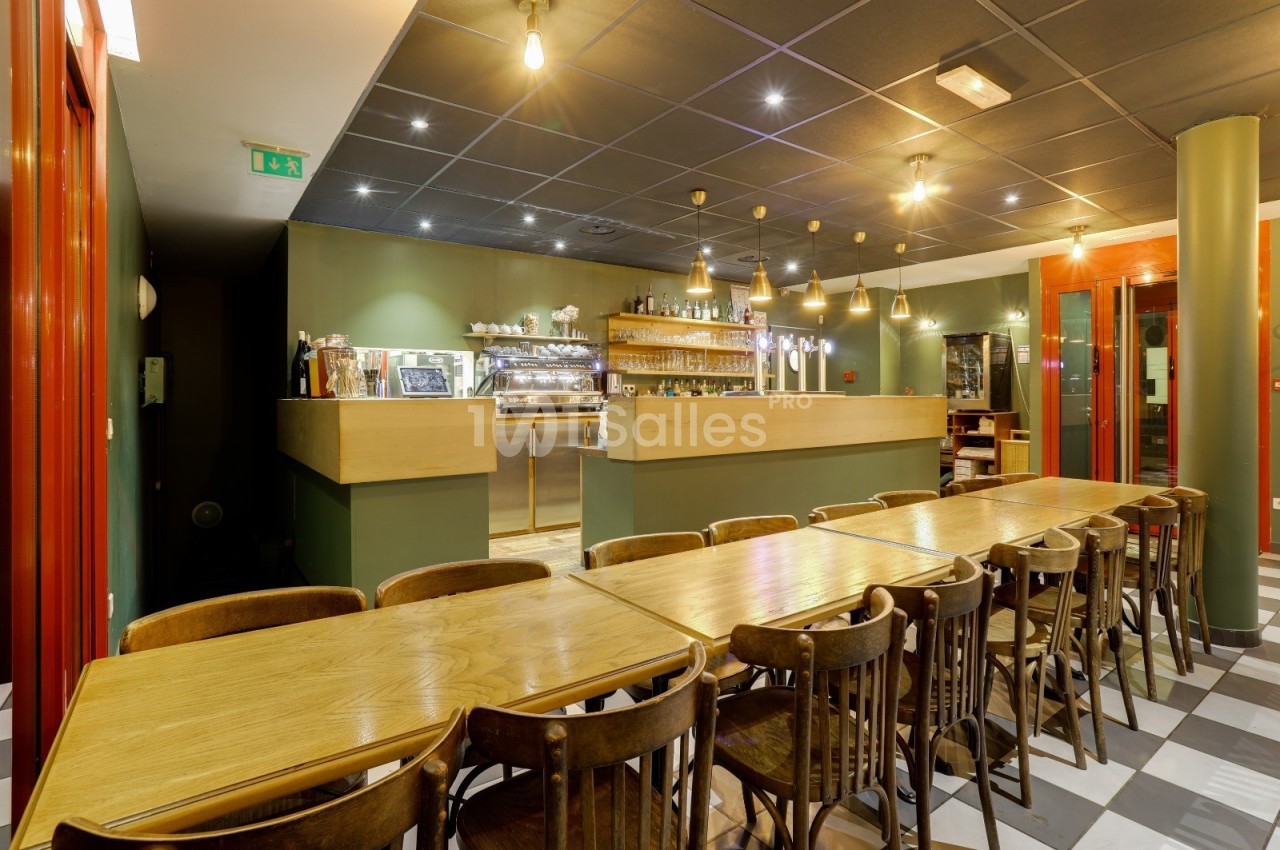 Salle de restaurant avec tables en bois alignées, chaises assorties et un comptoir éclairé en arrière-plan.
