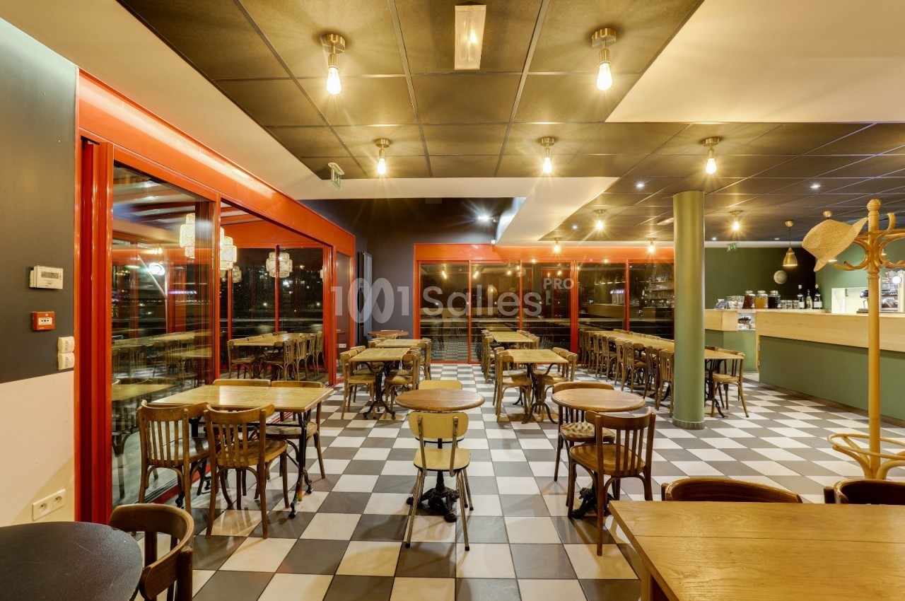 Salle de restaurant lumineuse avec tables en bois, chaises assorties et sol à carreaux noirs et blancs.