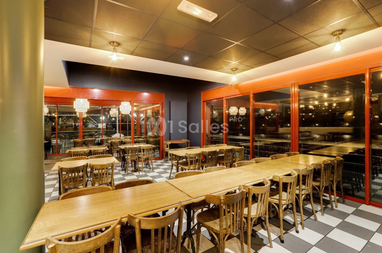 Salle de restaurant lumineuse avec de grandes baies vitrées, des tables en bois et des chaises assorties.
