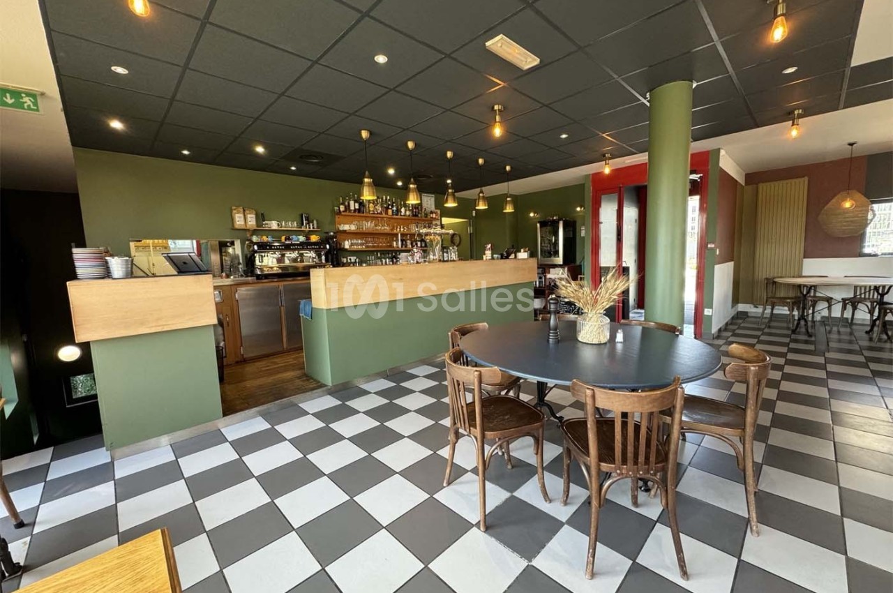 Salle de restaurant lumineuse avec un comptoir en bois, des tables et chaises en bois, et un sol à carreaux noirs et blancs.