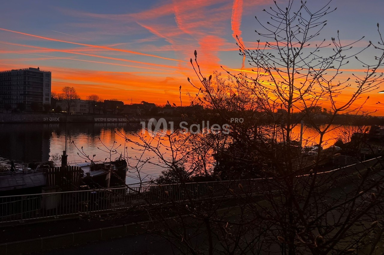 Coucher de soleil vibrant avec des nuages colorés se reflétant sur une rivière bordée d'arbres et de bâtiments.