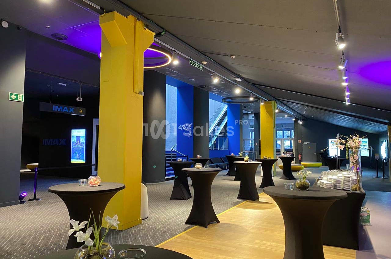 Salle moderne aménagée pour un événement, avec tables hautes noires, décorations florales et éclairage tamisé.